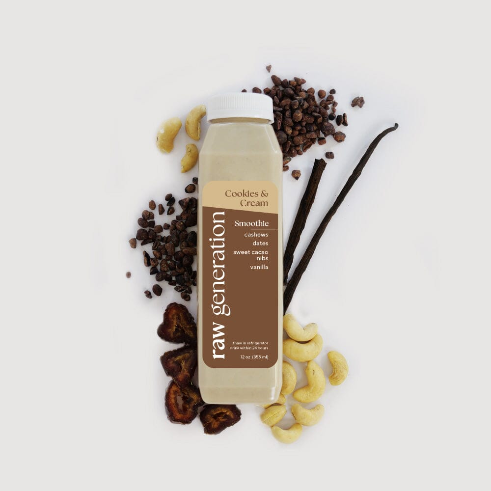 A Raw Generation Cookies & Cream Smoothie bottle rests on a white surface, encircled by raw cashews, cacao nibs, vanilla beans, and dates. The label features ingredients like cashews, dates, coconut, cacao, and vanilla for a tasty plant-based protein boost.