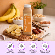 Peanut Butter Cup Smoothie bottle with cashews, banana, peanuts, dates, cacao, and vanilla on a board, emphasizing plant-based protein and fitness benefits.