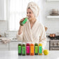 Beauty Box™ juices lined up on a kitchen counter, showcasing vibrant colors. A person sips a green juice, emphasizing the skincare routine's nourishing benefits.